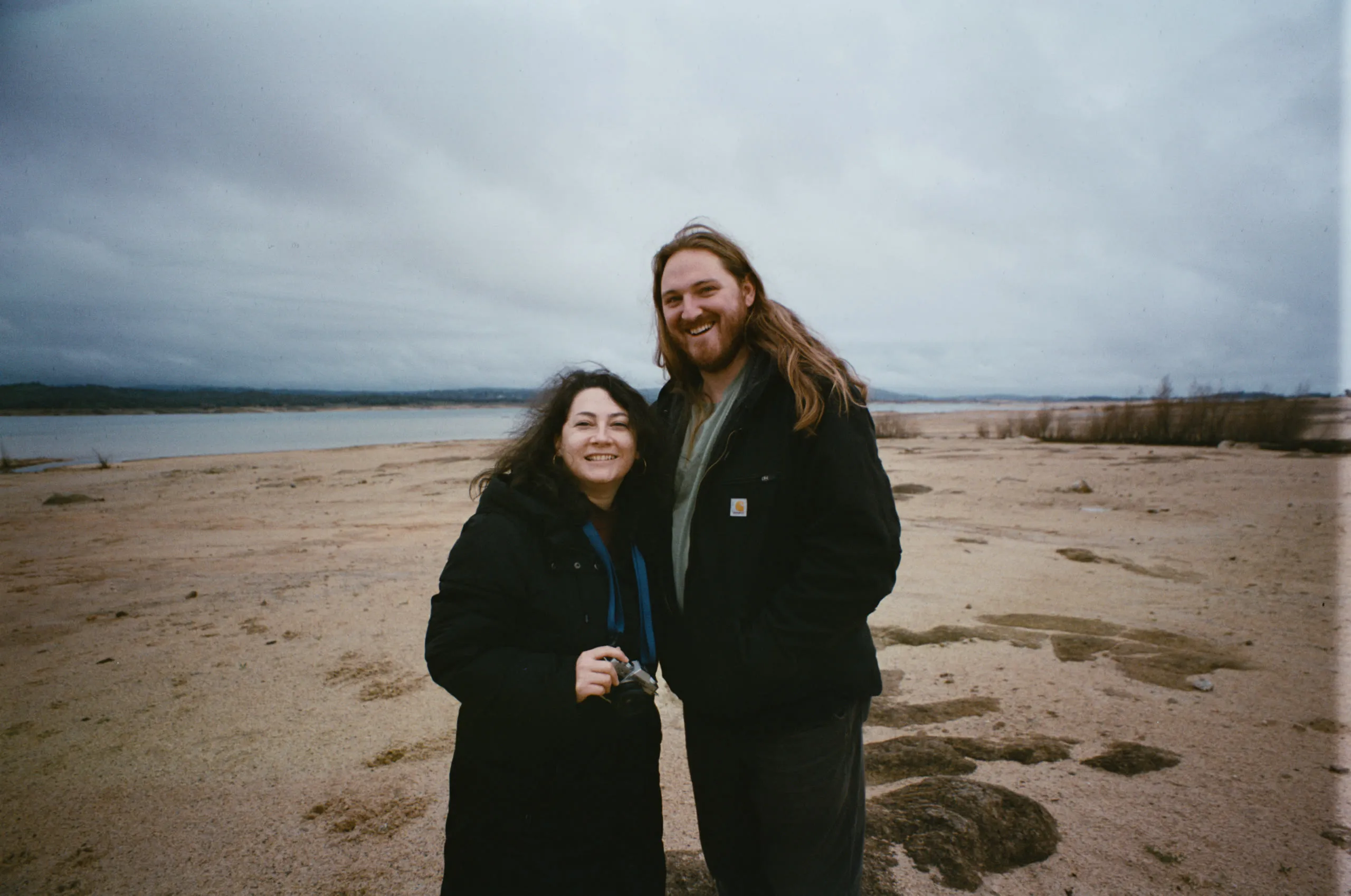 A couple on a wide estuary beach under a flat gray sky